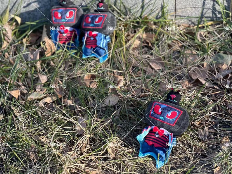 May include: Several plush robot-like figures with black bodies, red and blue accents, and antenna-like features are scattered on grass. The robots have rectangular faces with red eye designs and are wearing blue and red outfits.