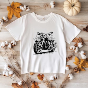 May include: White t-shirt with a black and white illustration of a motorcycle. The motorcycle has a large front wheel and a smaller back wheel.