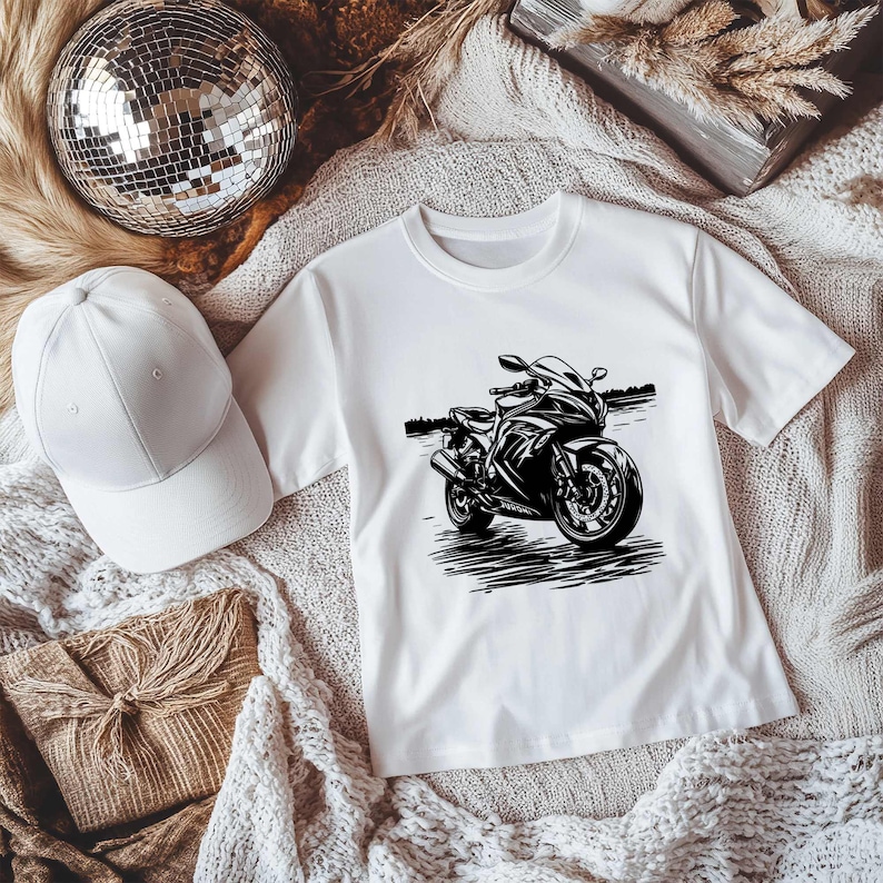 May include: White t-shirt with a black and white illustration of a motorcycle.