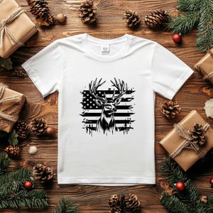 May include: White t-shirt with a black and white graphic of a deer with antlers standing in front of an American flag.