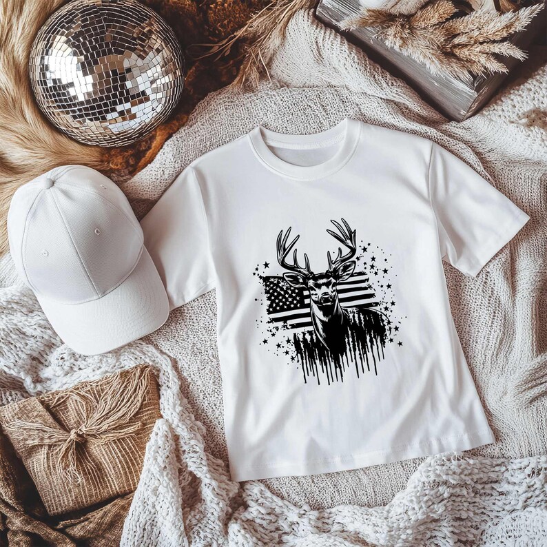 May include: White t-shirt with a black and white graphic of a deer with antlers standing in front of an American flag. The graphic is surrounded by stars.