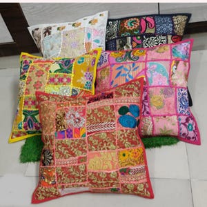 Peut inclure: Plusieurs coussins décoratifs avec des motifs patchwork. Les coussins présentent diverses couleurs, notamment le rouge, le rose, le jaune et le bleu, avec des motifs et des ornements complexes. Les coussins sont de forme carrée et semblent être en tissu.