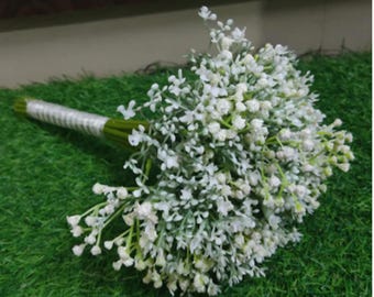 May include: A bouquet of white baby's breath flowers. The stems are wrapped in green tape and a white ribbon. The bouquet is set against a green background.
