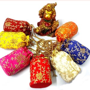 May include: A collection of colorful drawstring pouches in red, yellow, pink, orange, blue, and cream, each adorned with gold embroidery. A golden Buddha statue sits above the pouches. The pouches are arranged in a circular pattern.