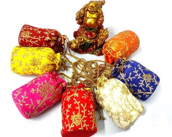 May include: A collection of colorful drawstring pouches in red, yellow, pink, orange, blue, and cream, each adorned with gold embroidery. A golden Buddha statue sits above the pouches. The pouches are arranged in a circular pattern.