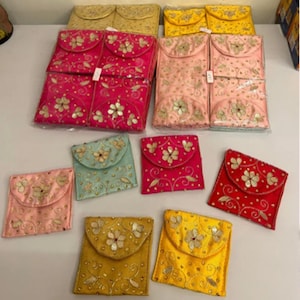 Op de afbeelding: Een assortiment kleurrijke, geborduurde stoffen zakjes in verschillende maten. De zakjes zijn in tinten roze, geel, goud, rood en blauwgroen, met bloemen- en krulwerkontwerpen. Sommige zakjes zijn opgevouwen, andere plat.