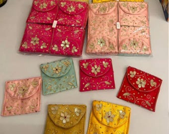 May include: An assortment of colorful, embroidered fabric pouches in various sizes. The pouches are in shades of pink, yellow, gold, red, and teal, with floral and scrollwork designs. Some pouches are folded over, while others are flat.