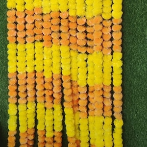 May include: A garland of yellow and orange marigold flowers, arranged in alternating rows. The garland is made of artificial flowers and is perfect for decorating for a special occasion.