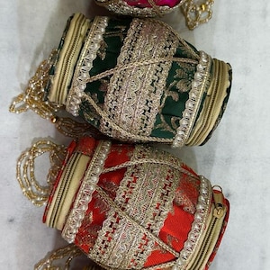 Op de afbeelding: Vier sierlijke, cilindrische portemonnees in levendige kleuren: fuchsia, groen, rood en geel. Elke portemonnee heeft ingewikkelde gouden borduursels, kralenaccenten en een ritssluiting. Een delicate kralenketting dient als handvat.