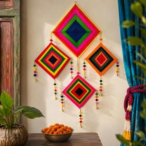 Può includere: Una decorazione da parete composta da quattro mandala di filo a forma di rombo interconnessi in colori vivaci tra cui rosa, verde, blu, arancione e giallo. Ogni rombo presenta fili pendenti decorati con piccoli pon pon colorati e campanellini dorati.