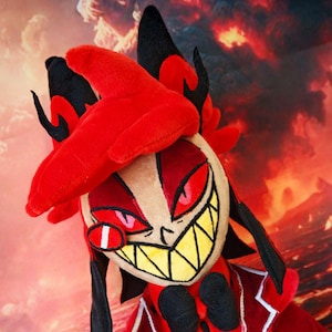 Può includere: Bambola di peluche di un personaggio rosso e nero. La bambola ha un cappotto rosso con finiture bianche, un papillon nero e un grande sorriso con denti gialli. Il personaggio ha occhi rossi e un monocolo.