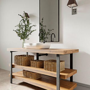 Puede incluir: Un mueble de baño con una encimera de madera gruesa y dos estantes inferiores sostenidos por un marco de metal oscuro. Un lavabo rectangular blanco con un grifo negro se asienta encima. Cuatro cestas de mimbre están en los estantes.