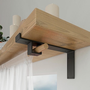 May include: A natural wood shelf mounted with a black metal L-shaped bracket that features an integrated square loop holding a horizontal wooden rod. A sheer white curtain hangs from the rod, and the shelf surface displays two ribbed candles.