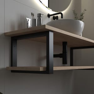 Op de afbeelding: Een moderne badkamermeubel met een lichte houten plank en een zwart metalen frame. Een witte, ovale wastafel staat erop, met een zwarte kraan. De meubel heeft een onderste plank en is aan de muur bevestigd.