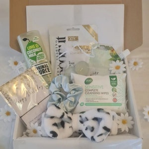May include: A white gift box filled with various self-care items, including a bottle of lime and coconut milk body wash, a face mask, a headband, a hair scrunchie, a pack of cleansing wipes, and a card that says "Happy Birthday".