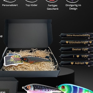 Könnte beinhalten: Eine schwarze Geschenkbox mit Holzeinlage, die einen personalisierten Angelköder mit einem "Reel Cool Dad" Aufkleber enthält. Die Box enthält außerdem eine Reihe schwarzer Geschenkanhänger mit goldener Beschriftung, darunter "Deine Wunschwidmung", "Glücksbringer", "Bester Opa", "I ♥ YOU" und "Adrian".