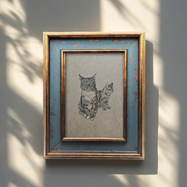 May include: A framed artwork featuring a pencil sketch of two cats. The frame has a distressed blue exterior with gold trim. The cats are depicted in a realistic style, with detailed fur patterns and expressions. The artwork is displayed on a neutral-toned background.