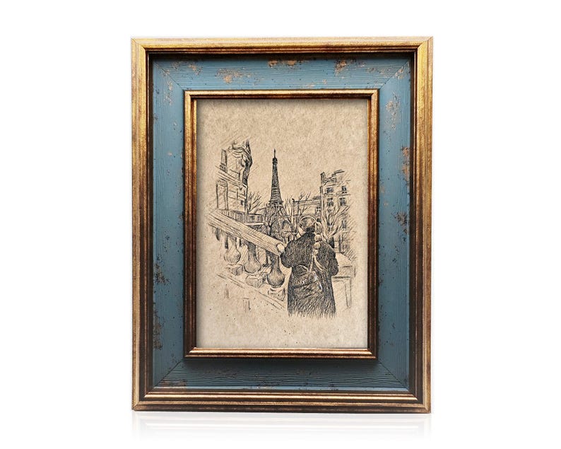 May include: A framed sketch of the Eiffel Tower and a person in Paris. The frame has a distressed blue outer edge and a gold inner edge. The artwork is in a rectangular format.