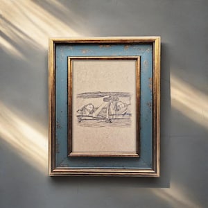 May include: A framed pencil sketch depicting two figures in a car, with a distressed blue and gold frame. The artwork shows a detailed drawing of the figures, suggesting a vintage or artistic theme. The frame adds a touch of elegance.