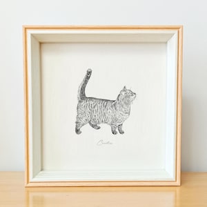 以下が含まれることがあります： 木製の額縁に入った猫の白黒の絵。猫は右を見ており、絵には「セシリア」と署名されています。