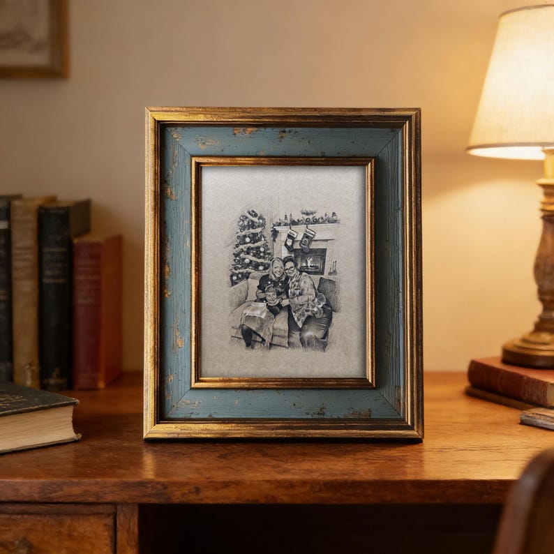 May include: A framed family portrait with a blue and gold distressed finish. The portrait is a pencil sketch of a family in front of a Christmas tree and fireplace. The frame is on a wooden desk with a lamp and books.