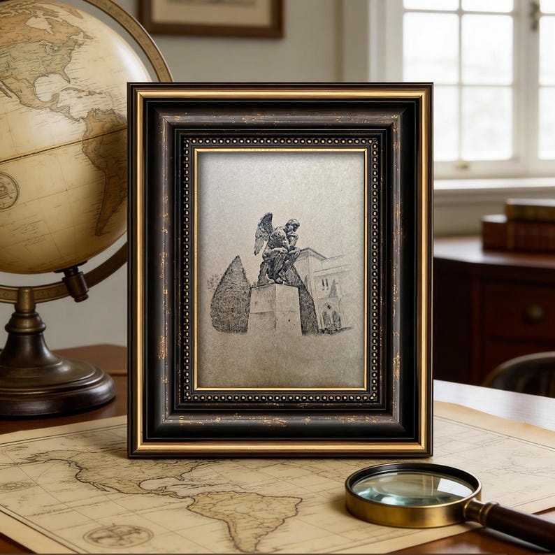 May include: A framed sketch of a statue with an angel figure, set in a black and gold ornate frame. The frame is displayed on a table with a vintage globe, a map, and a magnifying glass.