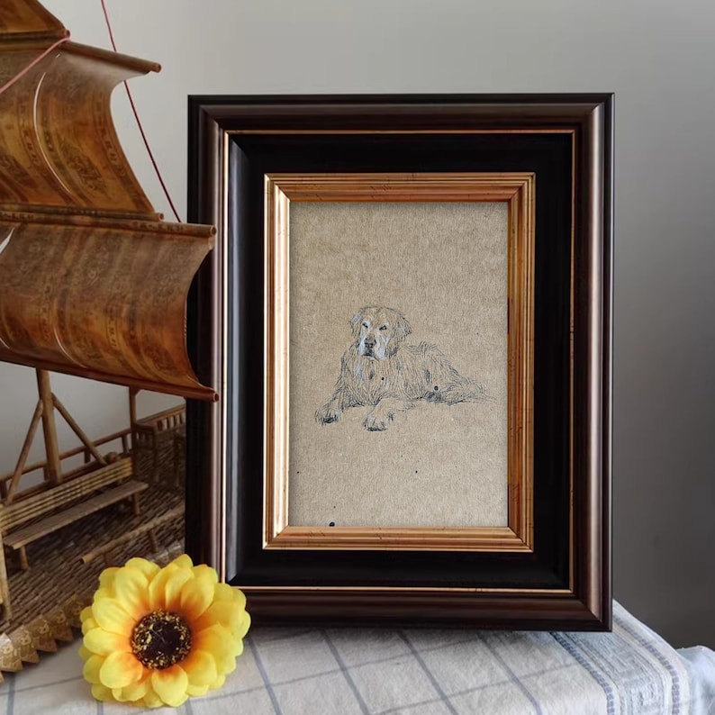 May include: A framed drawing of a golden retriever dog lying down. The dog is looking directly at the viewer. The drawing is on a beige background and is framed in a black and gold frame.