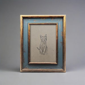 May include: A framed pencil sketch of a seated cat. The frame has a distressed blue finish with gold trim. The artwork is on a tan background, creating a vintage aesthetic. The cat is drawn in detail, with visible fur and facial features.