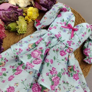 以下が含まれることがあります： ピンクのリボンと花柄のライトブルーのドレス。ドレスはフリルスカートとパフスリーブです。