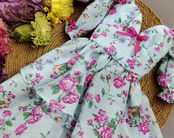 May include: A light blue dress with a pink bow and a floral print. The dress has a ruffled skirt and puffed sleeves.