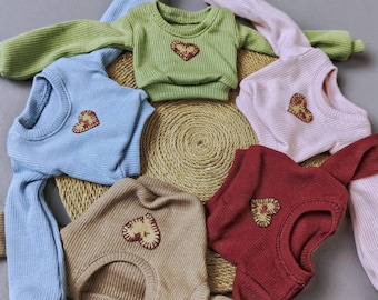 May include: Five long-sleeved sweaters with a heart-shaped patch on the front. The sweaters are in different colors: light blue, green, pink, brown, and red.