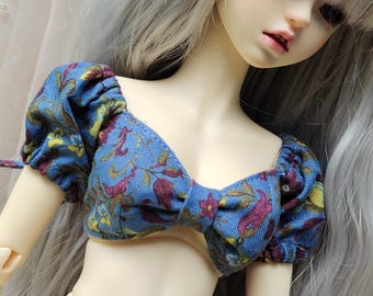 May include: A blue and burgundy floral print doll top with puffed sleeves. The top has a bow detail in the front.