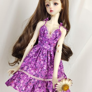 Peut inclure: Une robe à fleurs violettes avec un décolleté en cœur et des bretelles fines. La robe a un ourlet à volants et est faite d'un tissu doux et léger.