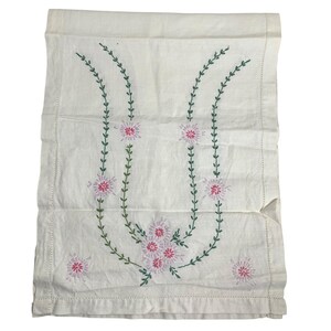 May include: Cream-colored linen towel with embroidered floral design. The embroidery features pink flowers and green stems arranged in a symmetrical pattern. The towel has a stitched border.
