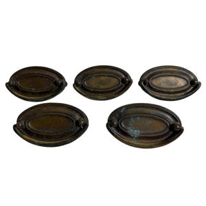 May include: Five antique bronze oval drawer pulls. Each pull has a raised oval center with rounded ends and small decorative knobs on each end. The pulls have a weathered, aged appearance.