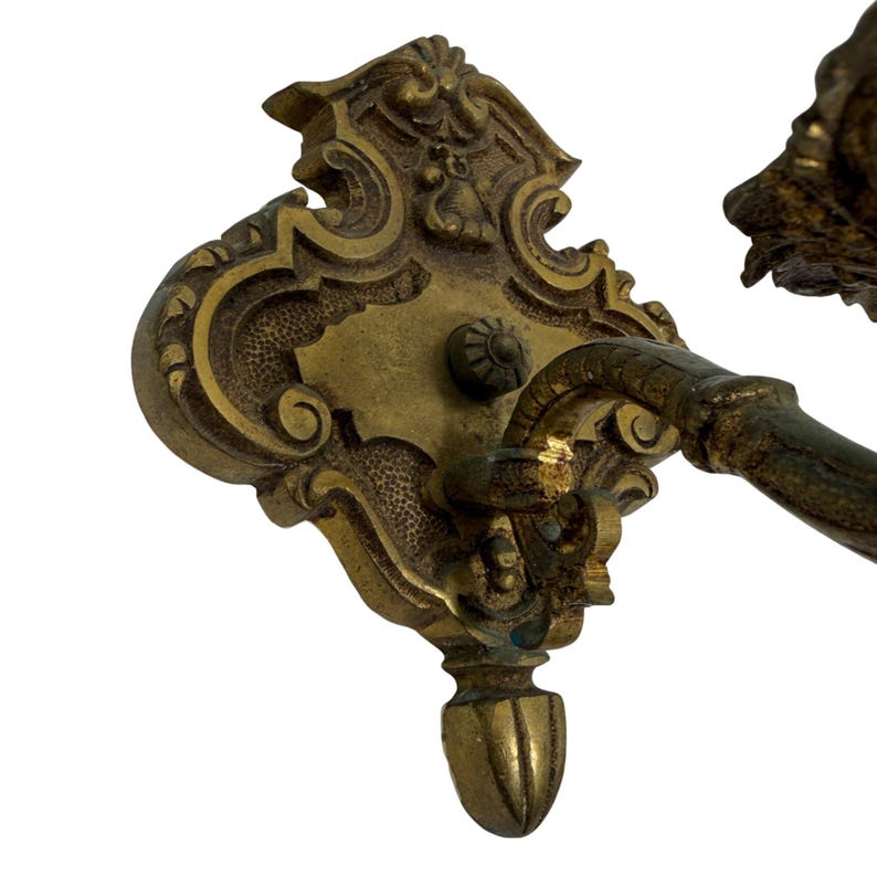 May include: Ornate antique brass door handle with intricate floral and scroll detailing. The handle features a decorative backplate and a curved lever. The brass has a warm, aged patina, suggesting its vintage origin. The handle is mounted on a white background.