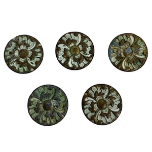 May include: Five antique bronze-colored cabinet knobs with a floral design. The knobs are round with a raised floral pattern in a contrasting light green and white color. The knobs are arranged on a white background.