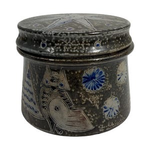 May include: A ceramic jar with a lid, featuring a dark gray speckled finish. The jar is adorned with an owl, a tree, and blue floral designs. The lid has a star pattern and blue accents. The jar is a decorative storage container.