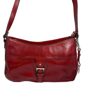 May include: A red leather shoulder bag with a silver buckle closure. The bag has a front pocket and a long, adjustable strap. The leather has a glossy finish.