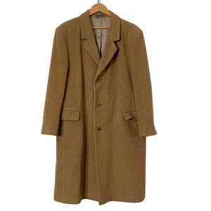 May include: A tan overcoat with a classic design, featuring a notched collar, three buttons, and two front pockets. The coat is hanging on a wooden hanger. The coat is made of a wool blend.