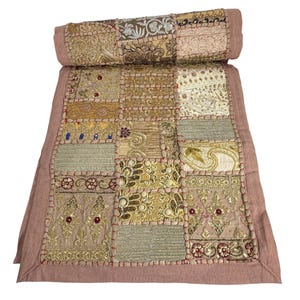 May include: A rectangular textile runner featuring a patchwork design of various embroidered fabrics in shades of gold, beige, and dusty pink. The piece is accented with metallic gold thread, sequins, and small red beads, finished with a solid pink border.