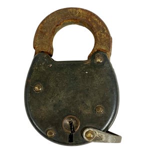 May include: Vintage Yale padlock with a dark, weathered finish. The metal lock features a rounded body, a U-shaped shackle, and the Yale brand name. The lock shows signs of age and wear, with a keyhole and a metal lever.