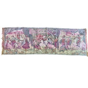 May include: A rectangular tapestry with a detailed scene of people in period clothing, possibly a festival or performance. The tapestry features a variety of colors, including pink, purple, and green, with a fringed edge.