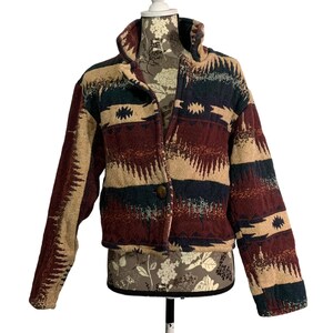 May include: A cropped jacket with a Southwestern-inspired pattern. The jacket features a high collar, a single-button closure, and long sleeves. The design incorporates beige, burgundy, navy, and teal colors with geometric and tribal motifs.