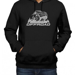 Puede incluir: Sudadera con capucha negra con un gráfico blanco de un jeep conduciendo por una cordillera con la palabra "OFFROAD" impresa debajo del jeep.