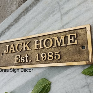 May include: A brass plaque with the text "JACK HOME Est. 1985" and the words "Braa Sign Decor" below.