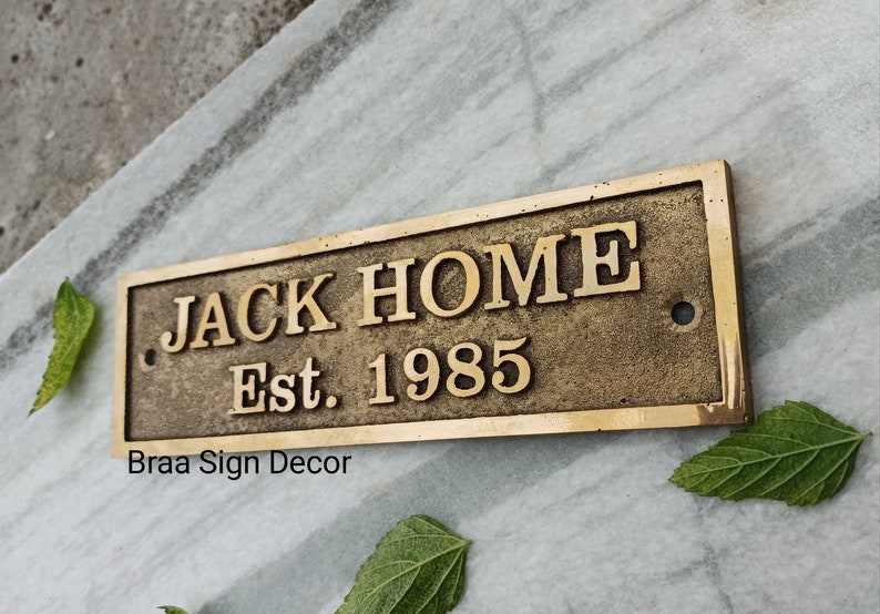 May include: A brass plaque with the text "JACK HOME Est. 1985" and the words "Braa Sign Decor" below.