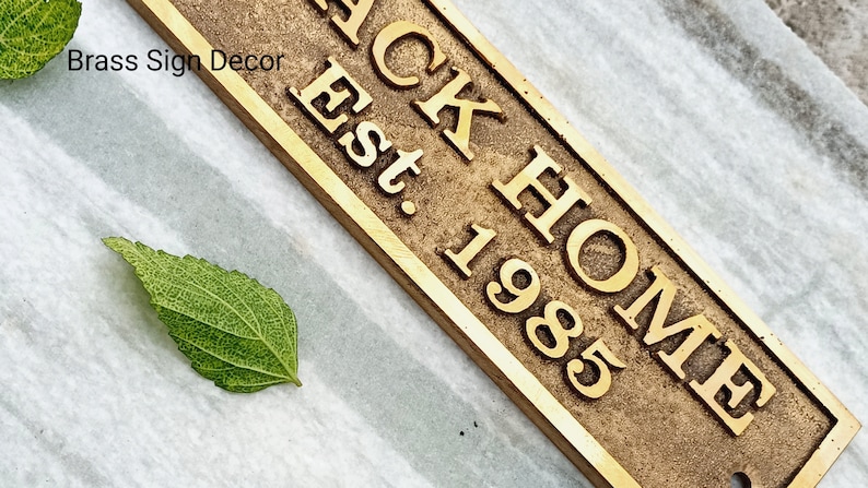 May include: A brass sign with the text "BACK HOME Est. 1985". The sign has a rustic, aged look.