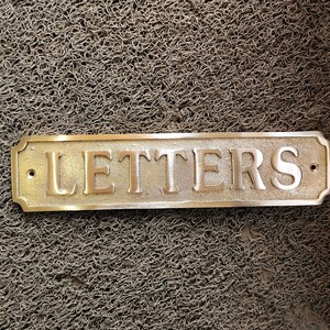 May include: A brass sign with rounded edges and a raised inscription that reads "LETTERS".