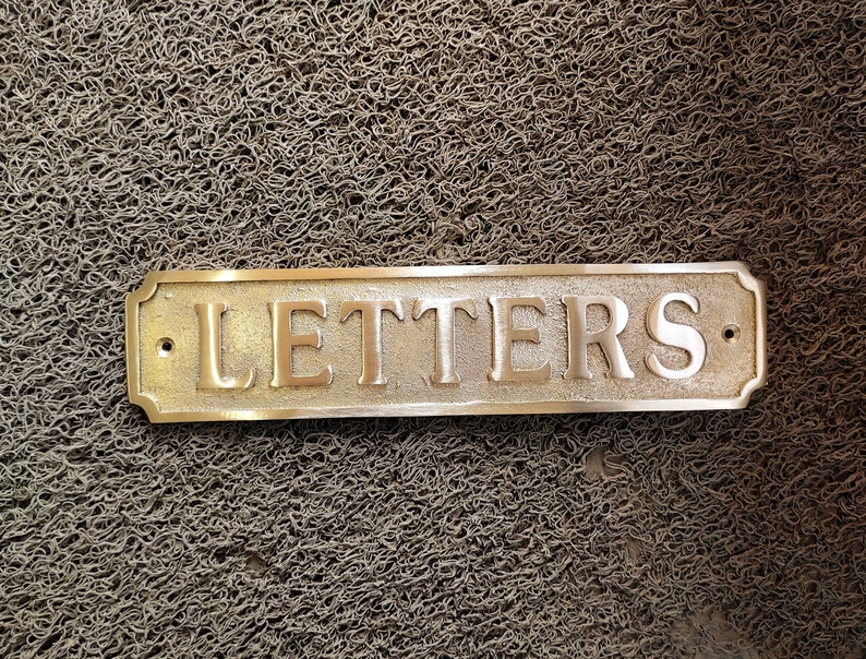 May include: A brass sign with rounded edges and a raised inscription that reads "LETTERS".